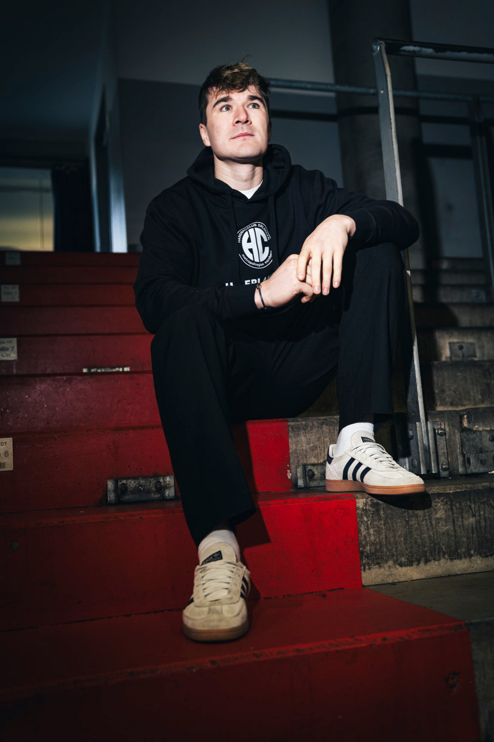 Yannik Bialowas im schwarzen HC Erlangen Classics Pullover auf der roten Hallentreppe