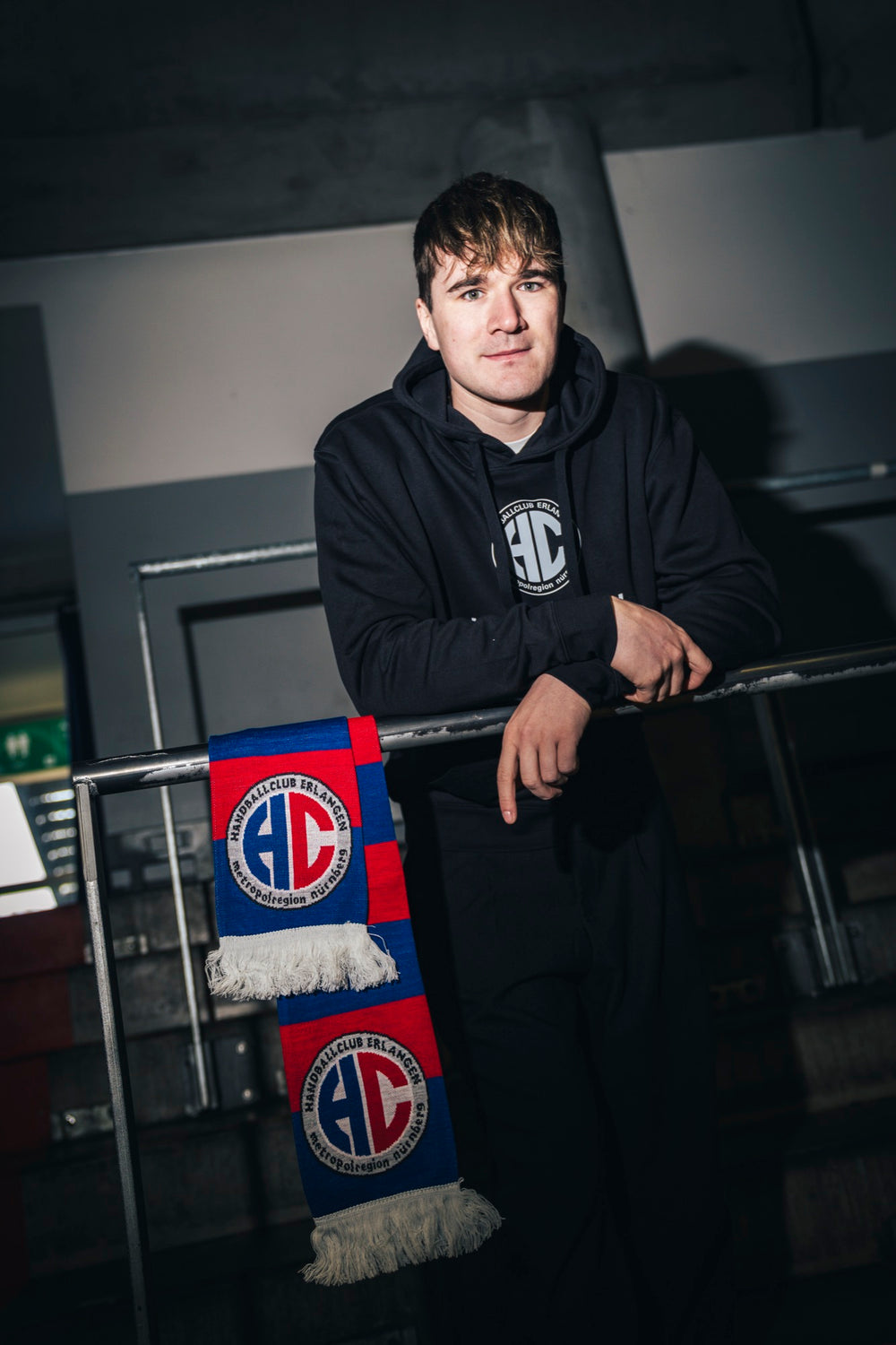 Yannik Bialowas im HC Erlangen Classics Pullover, daneben der HCE-Schal rot-blau